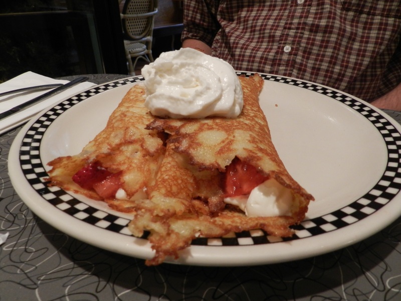 Hotcakes filled with strawberries, brown sugar, sour cream, and topped with whipped cream.